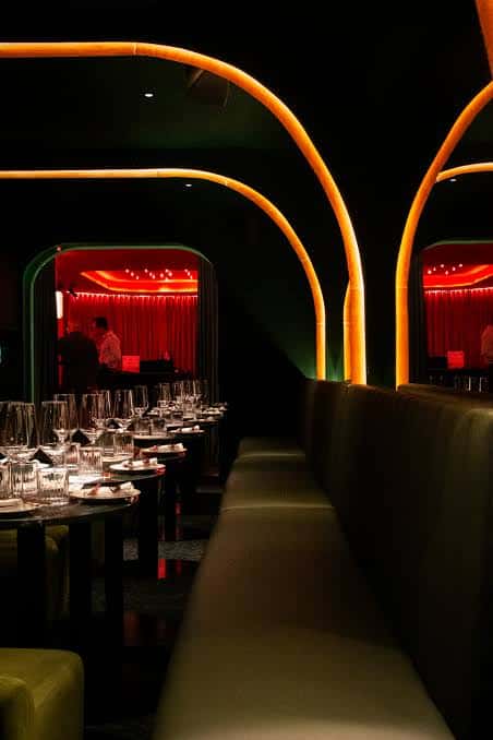 Sala de cócteles con mesas dispuestas y arcos iluminados en naranja