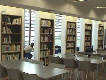 Interior de la biblioteca con estanterías llenas de libros y mesas de lectura