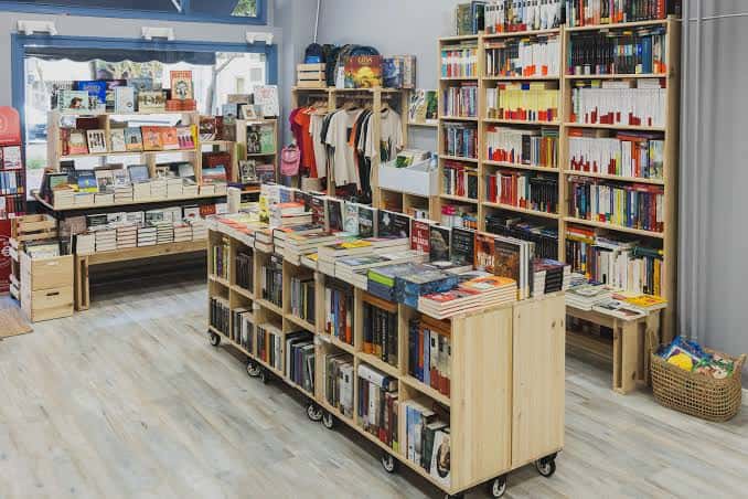 Área central de la librería con mesas móviles de libros y ropa en exhibición