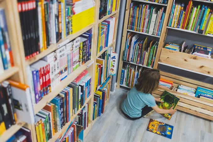 Niña explorando libros infantiles entre estanterías bajas