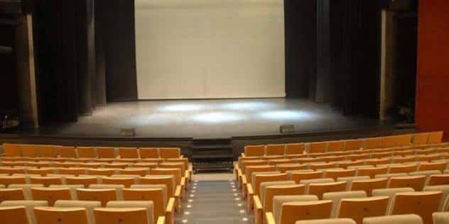 Escenario vacío con pantalla blanca y butacas naranjas en el auditorio