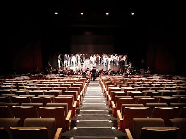 Auditorio lleno durante un ensayo general con grupo en escena y orquesta