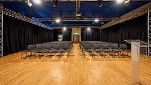 Aula magna con butacas dispuestas en filas y podio frente al escenario