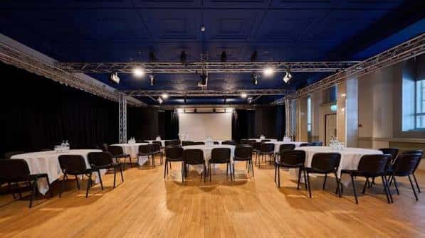 Gran salón con mesas rectangulares cubiertas y sillas negras bajo techo azul