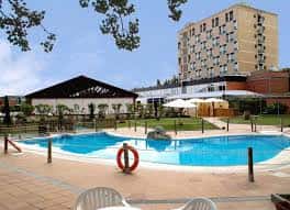 Piscina exterior del hotel con zona de descanso, sombrillas y edificación moderna al fondo