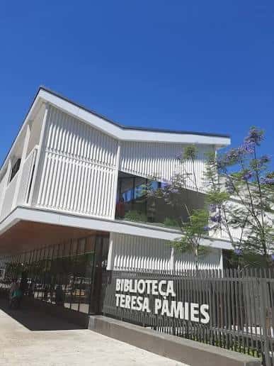 Fachada exterior de la Biblioteca Teresa Pàmies con letrero visible bajo cielo azul