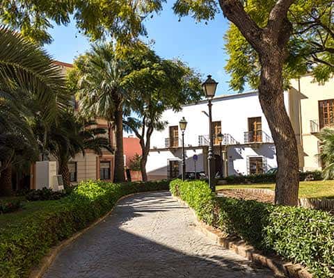 Sendero empedrado en el centro de la plaza rodeado de vegetación y farolas antiguas
