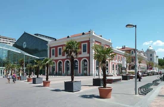 Vista exterior del edificio histórico de la estación con fachada neoclásica y plaza ajardinada