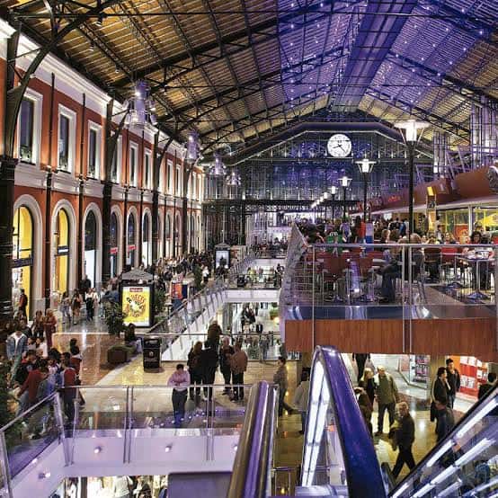Interior del centro comercial en la estación con techo de cristal iluminado y ambiente festivo