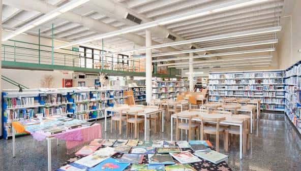 Interior principal de la biblioteca con estanterías, mesas de lectura y zona infantil