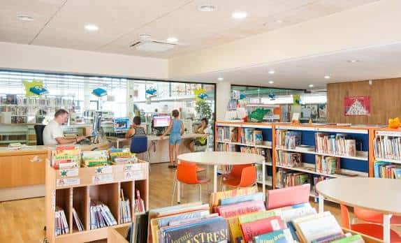 Área de préstamo y consulta con personal atendiendo a usuarios y libros expuestos