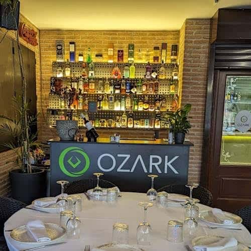 Bar del restaurante Ozark con estantería de botellas iluminada y mesa preparada