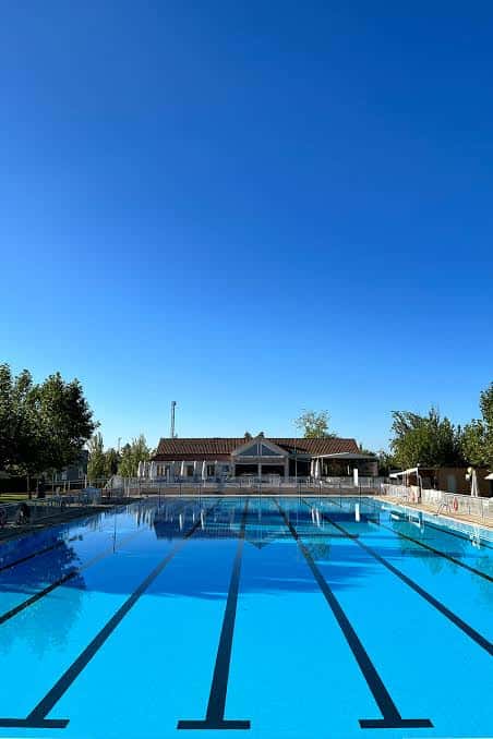 Piscina olímpica al aire libre con edificio deportivo al fondo bajo cielo despejado