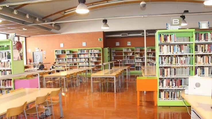 Interior de la sala de lectura con estanterías verdes y mesas de estudio