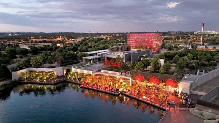 Vista nocturna de la Ciudad Financiera con iluminación cálida y eventos al aire libre junto al lago