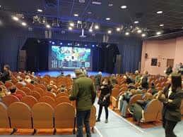 Interior del auditorio con butacas naranjas y escenario iluminado