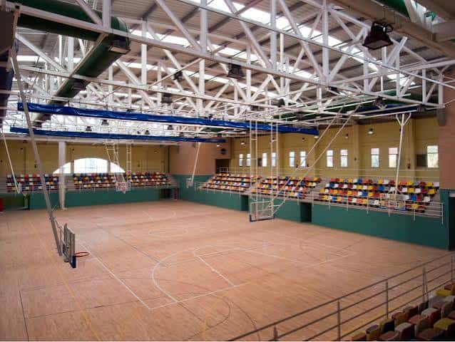 Vista interior del polideportivo con cancha de baloncesto y gradas multicolores