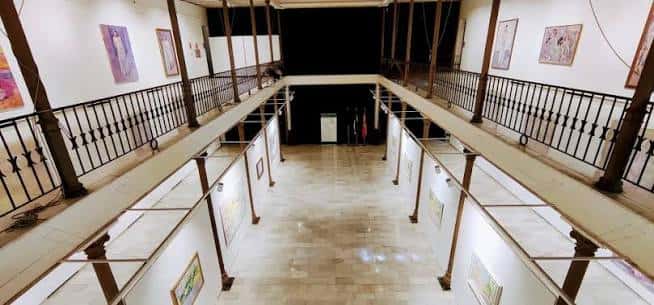Interior del teatro mostrando el vestíbulo con galerías superiores y exposición de cuadros