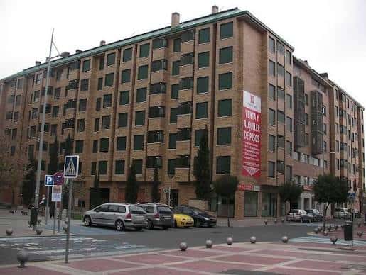 Fachada del edificio principal junto a la plaza con cartel de alquiler