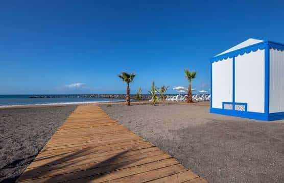 Pasarela de madera que conduce a la playa con caseta azul y blanca