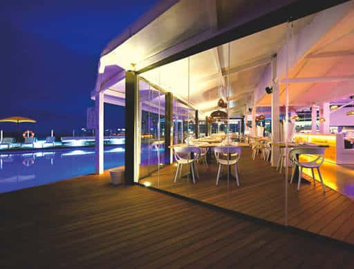Interior iluminado del club por la noche con mesas junto a la piscina y ambiente festivo