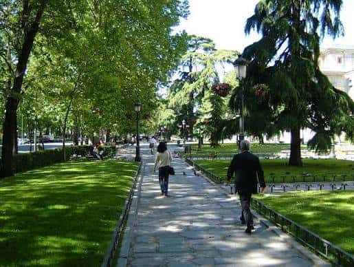 Paseo arbolado del Prado con personas caminando entre césped y farolas