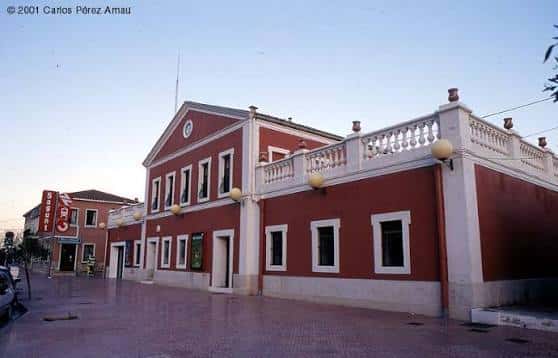 Vista lateral del edificio de la estación con balcón decorativo y farolas amarillas