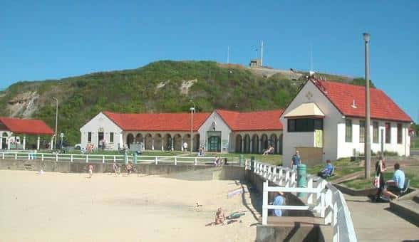 Fachada principal del complejo con edificios de techo rojo junto a la playa