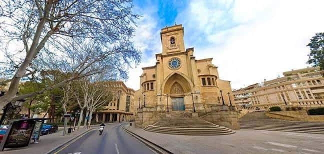 Panorámica exterior de la catedral desde la plaza, mostrando su entorno urbano y árboles en primer plano