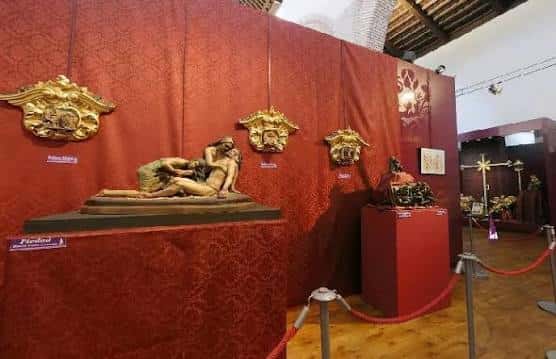 Exposición de arte sacro con esculturas barrocas sobre fondo rojo
