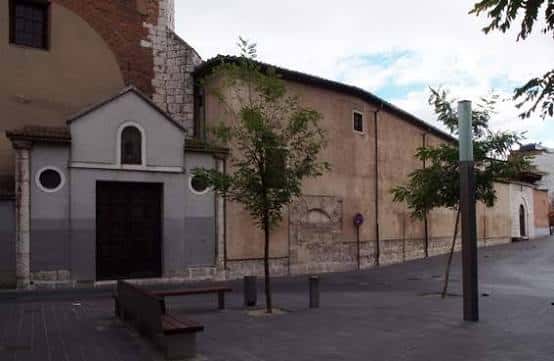 Fachada lateral del monasterio con árboles y banco en la plaza