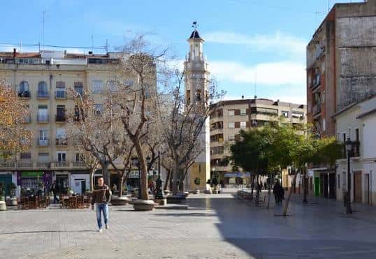 Vista amplia de la plaza con el campanario al fondo y personas caminando
