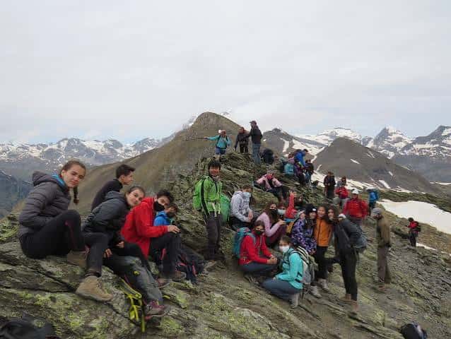 Multitud de montañeros descansando sobre las rocas del pico con vistas a los Pirineos al fondo