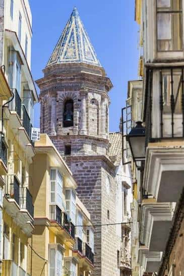 Torre campanario de la iglesia con cubierta cónica de azulejos entre edificios urbanos