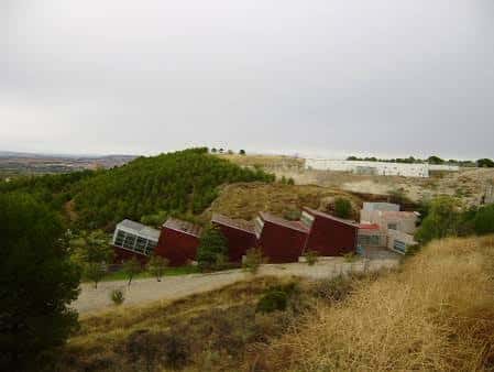 Panorámica del centro ambiental en su entorno natural, con edificaciones rojas integradas en la colina