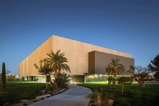 Fachada del edificio al atardecer con iluminación ambiental y jardines circundantes