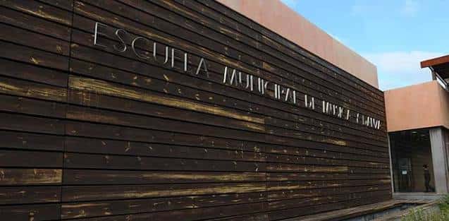 Fachada de madera oscura con el nombre de la escuela en letras metálicas