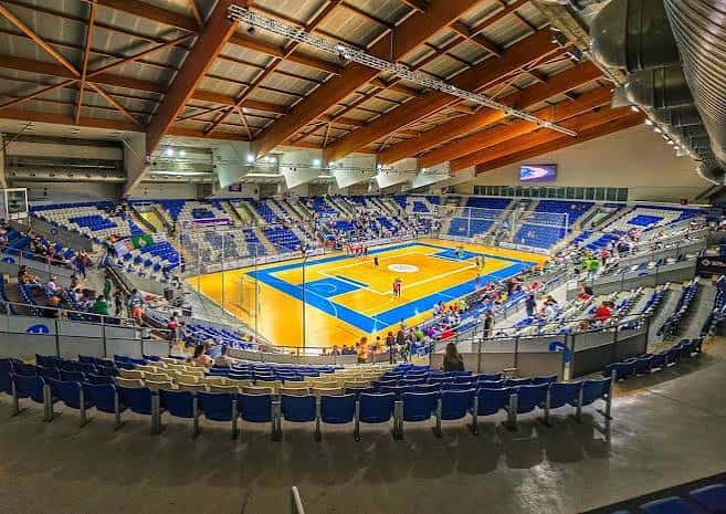 Vista panorámica del interior del pabellón con cancha de baloncesto y gradas azules