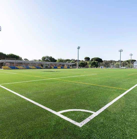 Campo de fútbol exterior con césped artificial y gradas bajo un cielo despejado