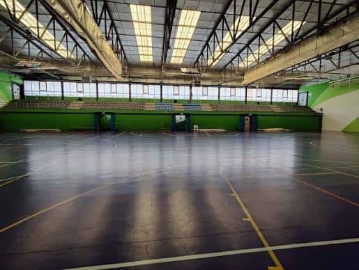 Pabellón deportivo interior con pista de baloncesto y gradas verdes