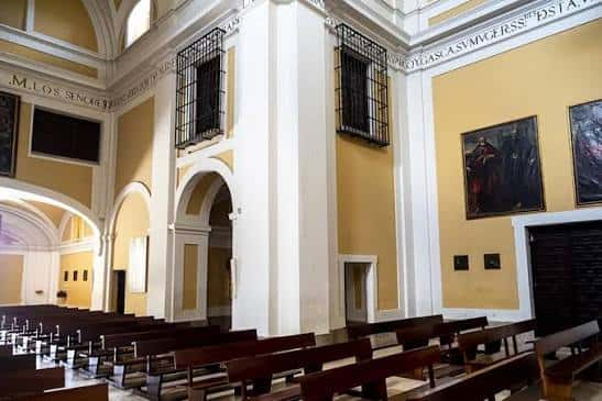 Interior de la iglesia con bancos de madera y paredes amarillas decoradas con pinturas religiosas