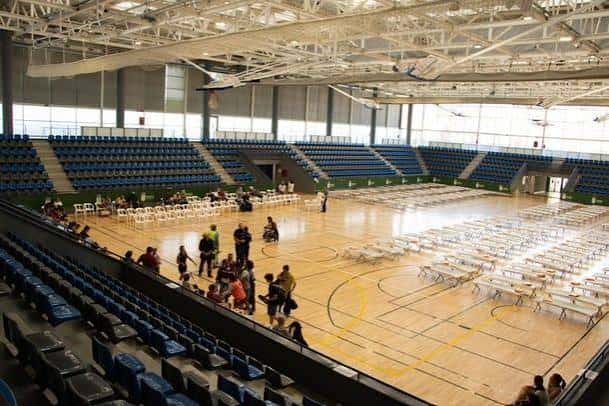 Interior del polideportivo configurado para evento con mesas y sillas blancas