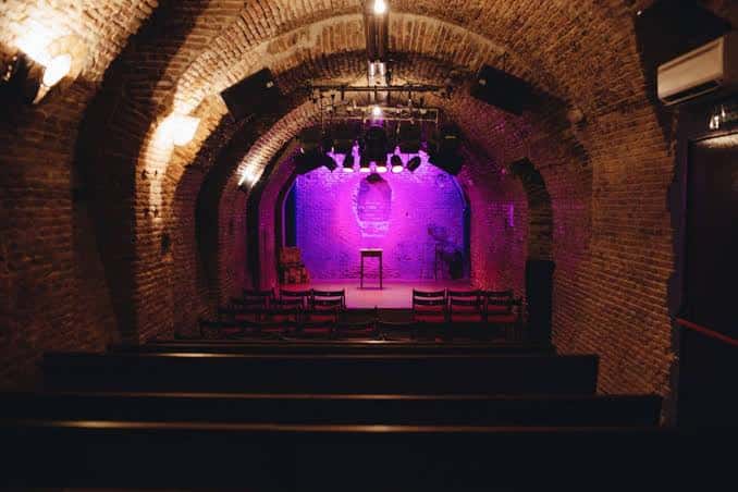 Vista del interior del teatro con paredes de ladrillo y escenario iluminado en morado