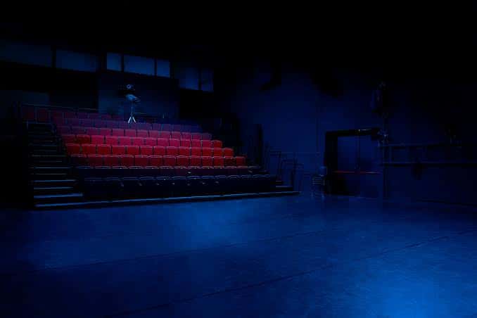 Interior de la sala con gradas de asientos rojos y escenario iluminado
