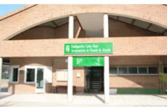 Entrada frontal del polideportivo con letrero verde y estructura de ladrillo