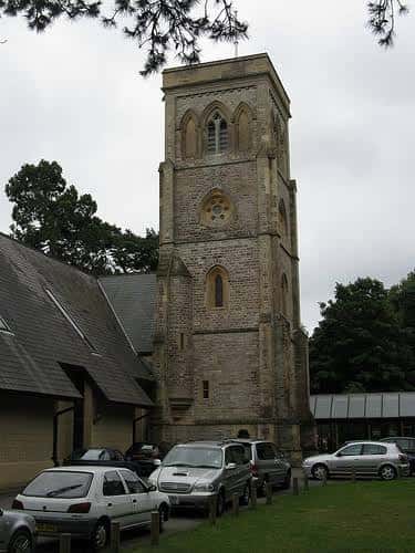 Torre de piedra de la iglesia con detalles arquitectónicos góticos y coches aparcados al frente