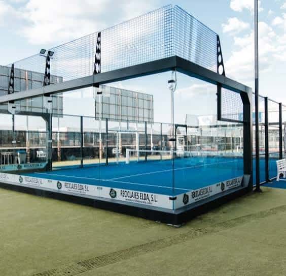 Pista de pádel exterior con superficie azul y vallas de cristal en Pádel Lacy