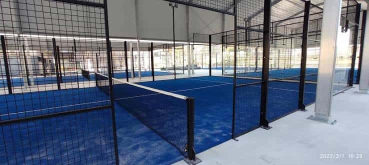 Interior de pista de pádel con iluminación artificial y suelo sintético azul