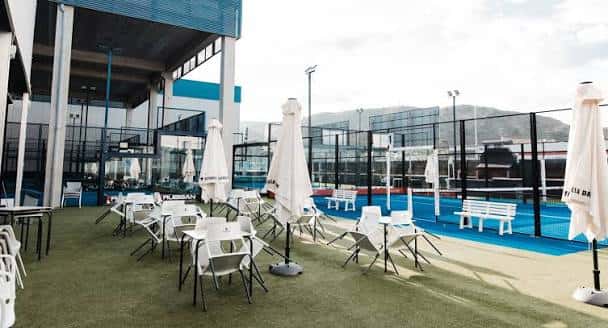 Zona de terraza con mesas, sillas y sombrillas junto a las pistas de pádel