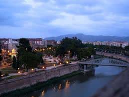 Vista panorámica de la Avenida del Río Segura al atardecer con el puente y las luces encendidas